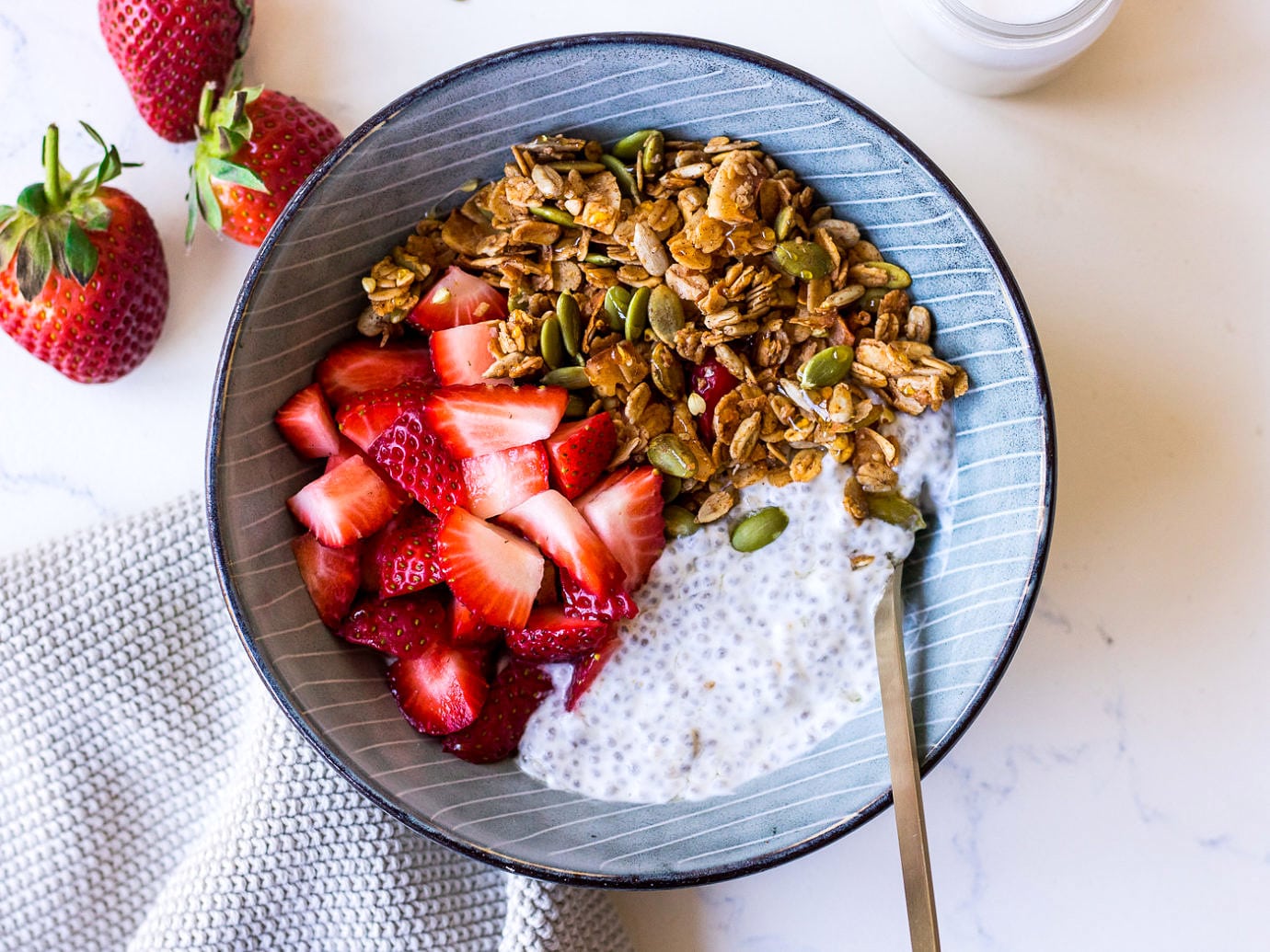 Blue bowl with chia pudding, chopped strawberries and granola, small gold spoon