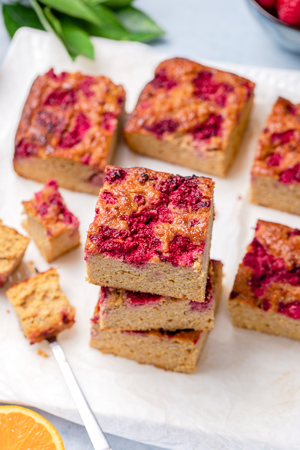 Square slices of orange almond and raspberry cake stacked with extra cake and berries